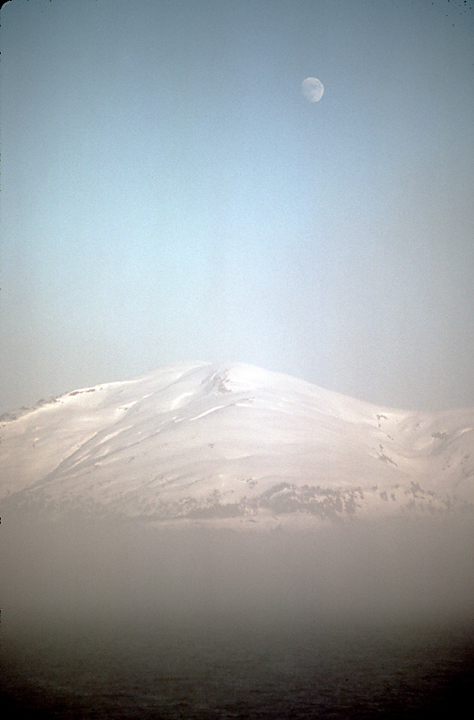 moon in light blue sky over snowy mountain in alaska