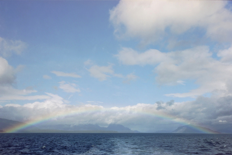 full rainbow over wavey water blue sky a few white clouds