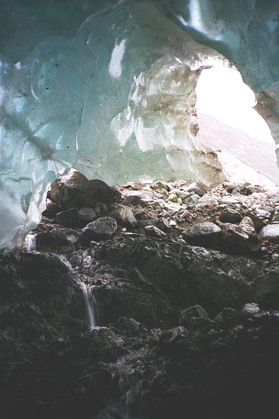 inside blue Ice Cave with white light door out, rocks in front and small waterfall