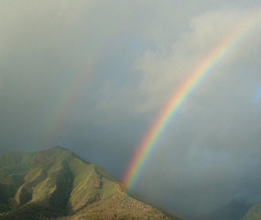 double rainbow in cloudy blue sky over mountain