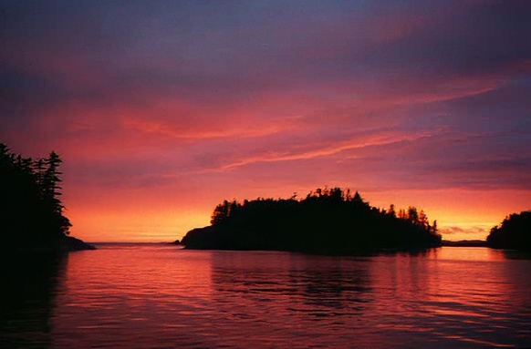 red and orange sunset reflected in water with dark island in center