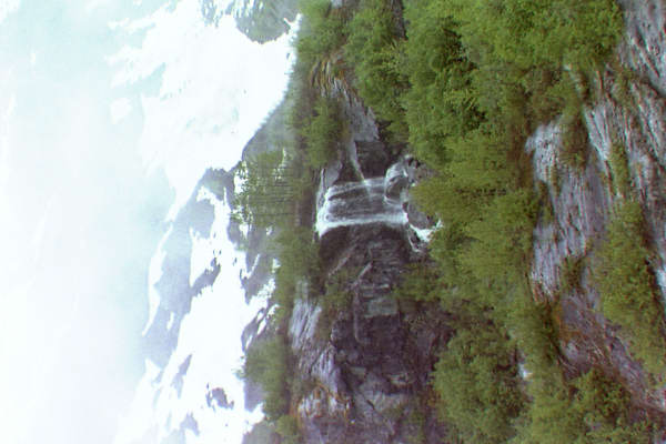 pretty waterfall with snow covered mountains and green trees